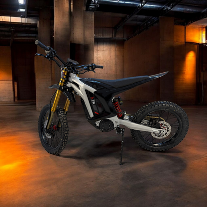 A sleek white and black electric dirt bike with gold front forks and red wheel accents, set on a high-clearance frame, surrounded by a misty, fog-filled background.